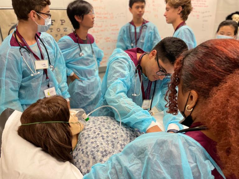 Students in hospital gowns practicing medicine on a dummy