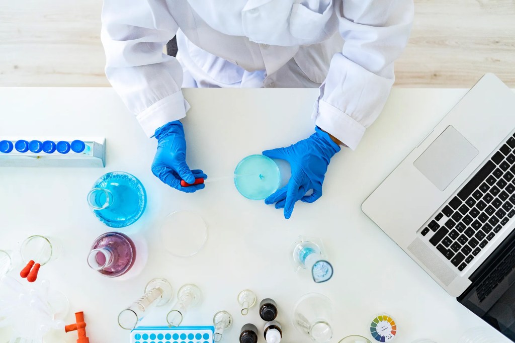 Person working in a lab with blue gloved and white scrubs.