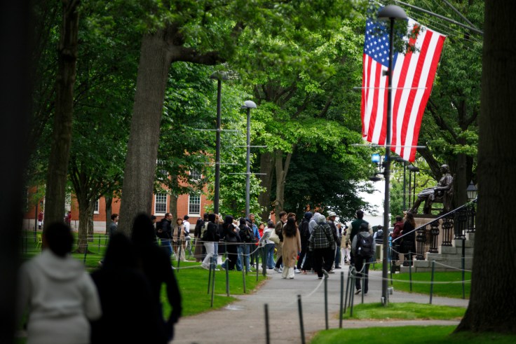 Visitors walk past the John Harvard statue and an American flag.