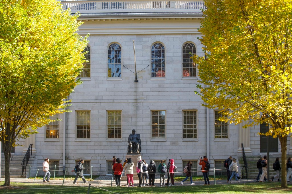 people standing in front of the John Harvard flanked by trees.