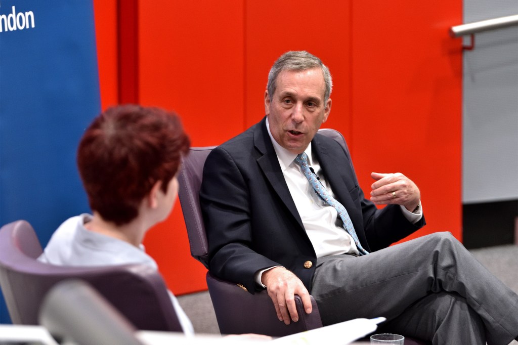 Larry talking with a woman on a stage in front of a red curtain.