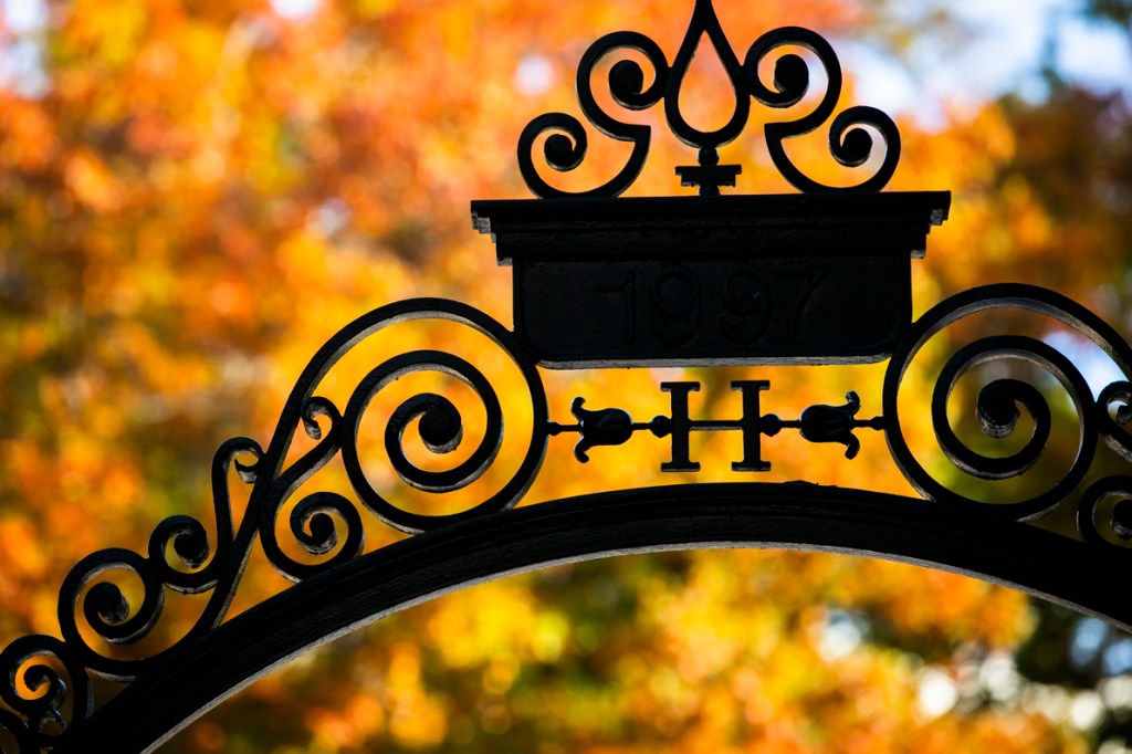 Fall leaves are on display alongside a gate decorated with an “H” at Harvard University.