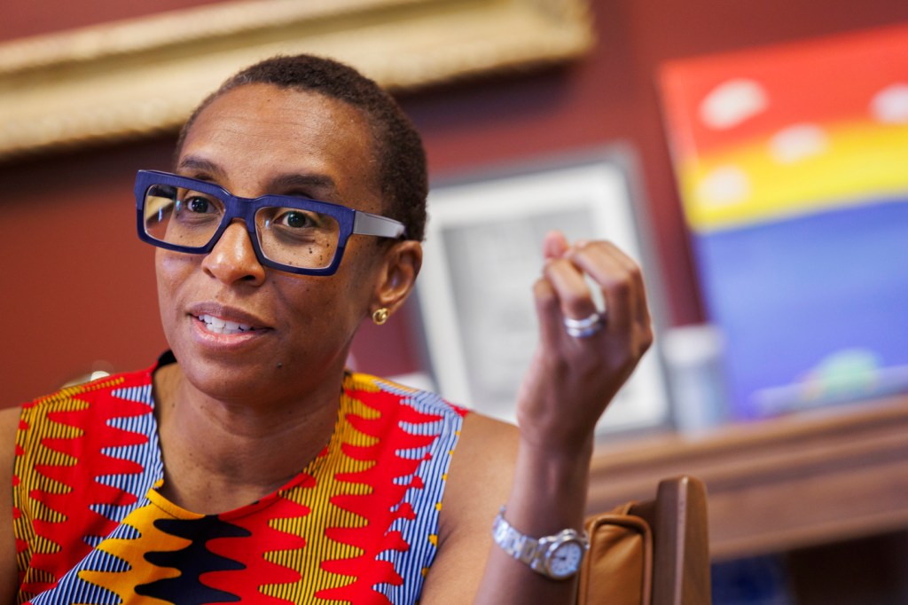 Claudine in a bright, multicolored shirt speaking to an interviewer