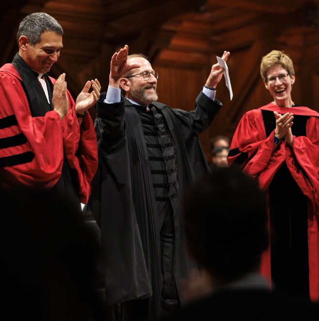 President Garber standing on stage in robes, with his hands over his head.