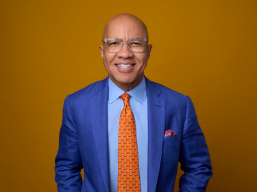 Man in a suit smiling with a yellow background.