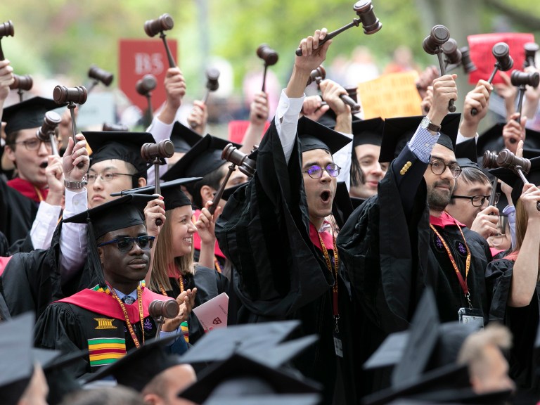 A crowd of students in graduation garb with gavels cheering.