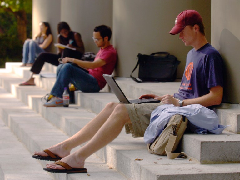 A male student sitting on steps with a laptop.