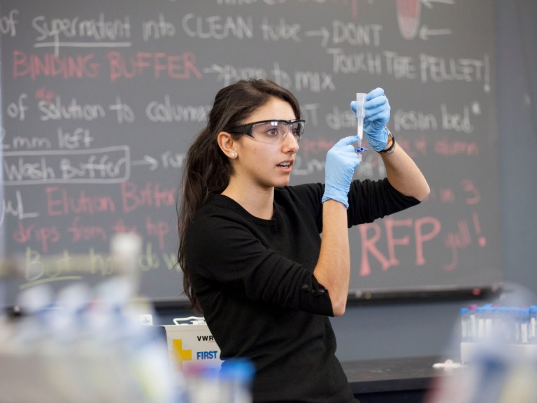 Woman wearing goggles and gloves holding a vial