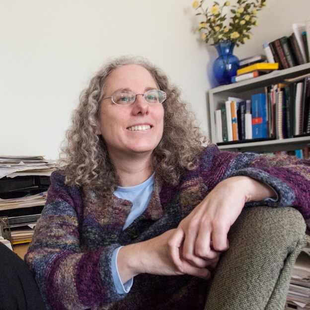 A woman sits in an office with books behind her