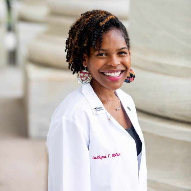 A medical school students stands outside wearing her white coat