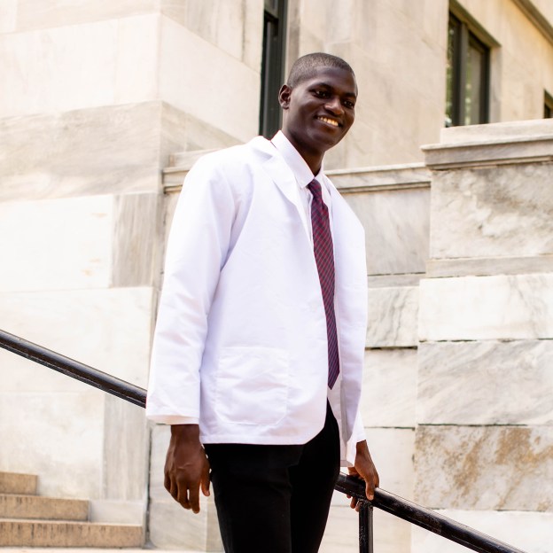 A medical school student wearing a white coat stands on stone steps