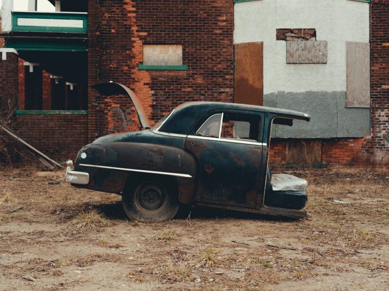 Half a car sitting behind a boarded up building