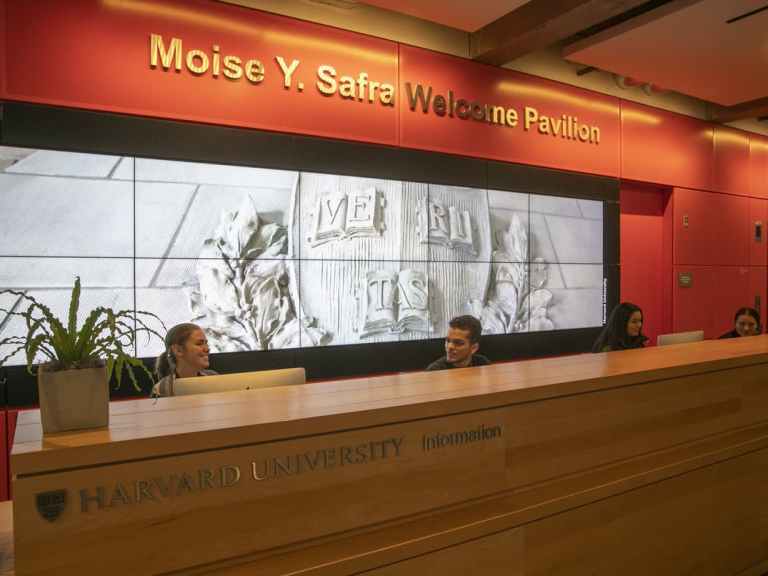 Students sitting at the information desk in front of a bright orange wall and screen.