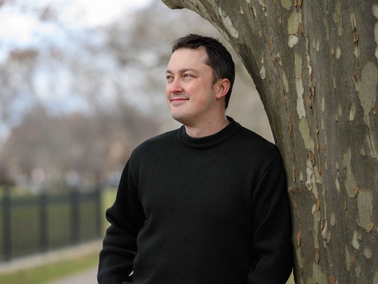 A man leans against a tree outside