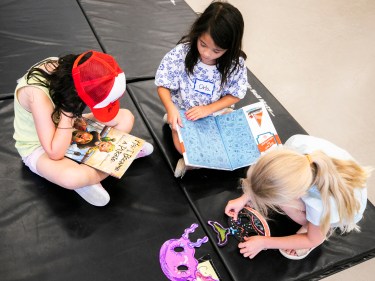 Three children play on the floor together during a summer drama class