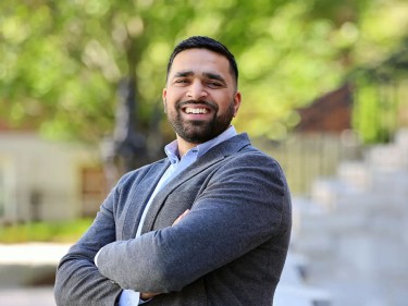 A man stands outside, smiling with his arms crossed.