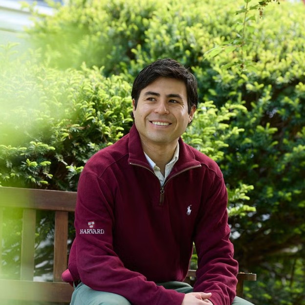 A student wearing a crimson Harvard jacket sits outside.
