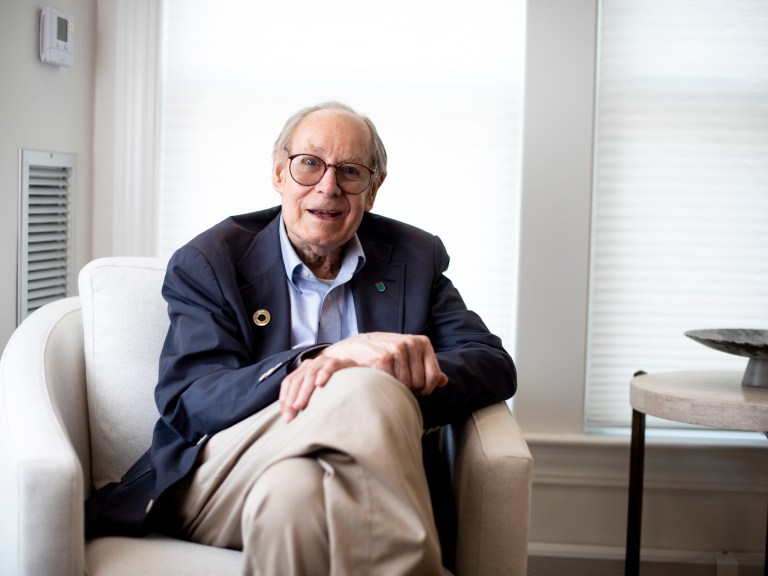 A man in a blue sport coat sits on a white armchair.